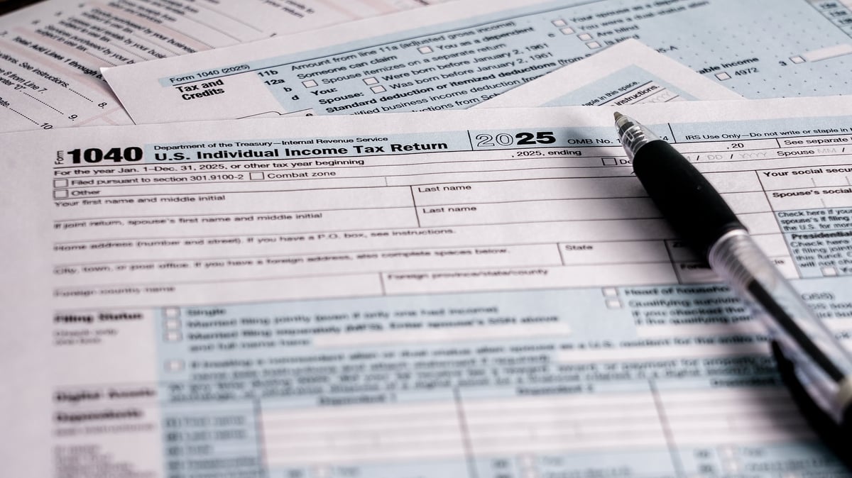 A person works on a U.S. individual income tax return with tax forms and a pen spread out on a table