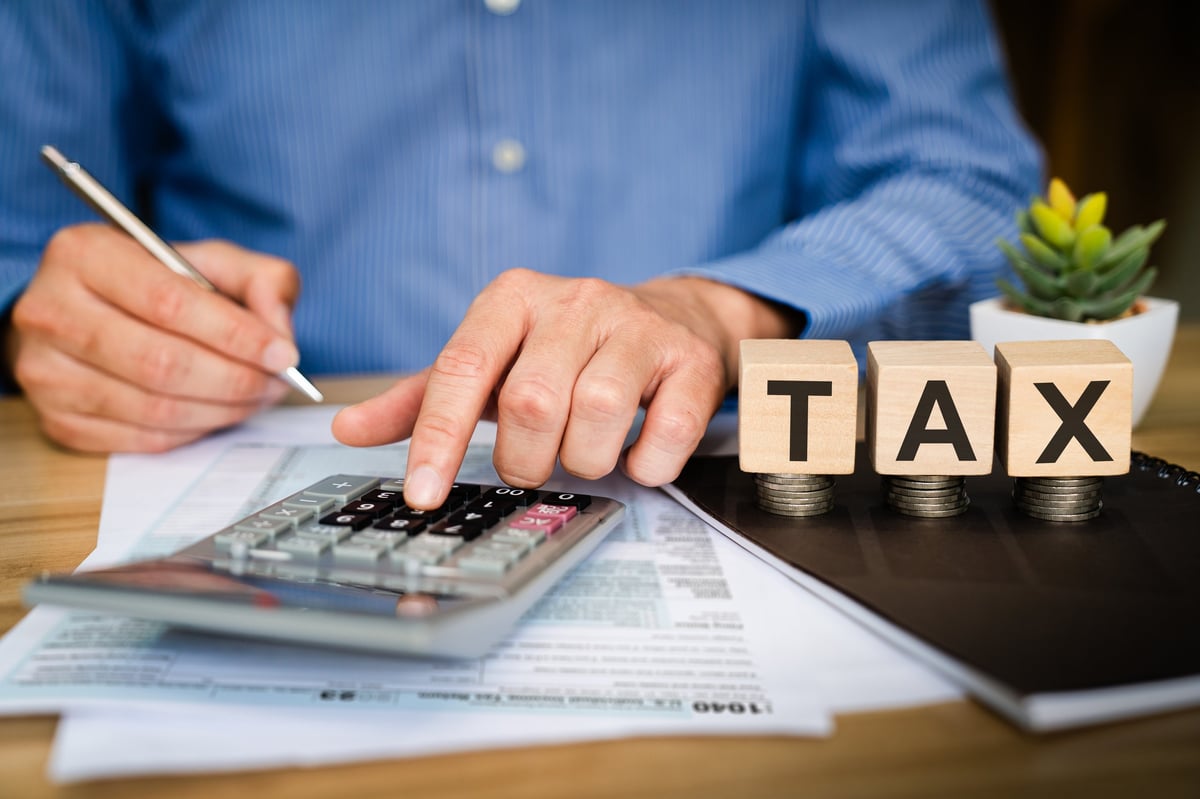 Tax professional calculating figures with a calculator beside wooden TAX blocks