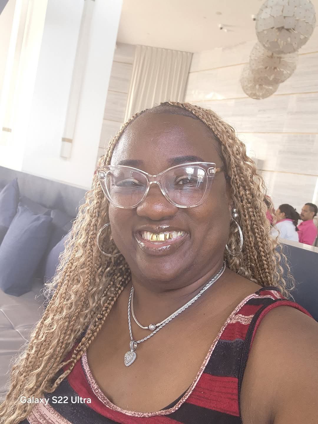 Woman smiling at the camera wearing clear-frame glasses, a necklace, and a red and black striped top at an indoor event