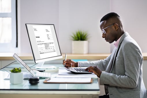 Man in glasses working at a desk with a laptop and documents in a business office setting