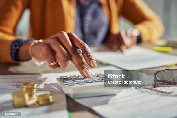 Woman wearing an orange cardigan typing on a calculator at a desk with financial documents and glasses